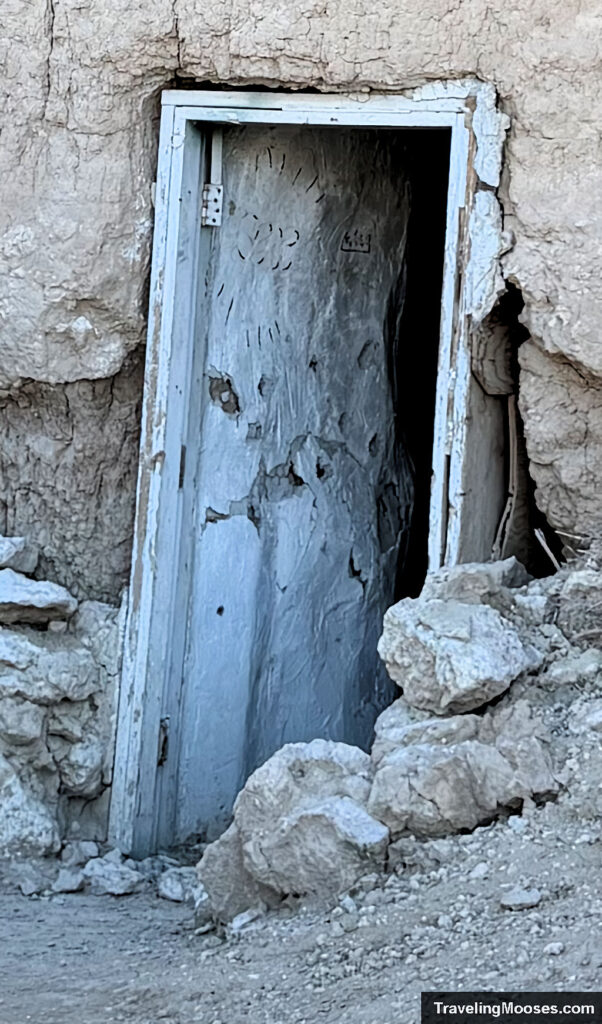 Vandalised and decaying white door leading into a mountain side