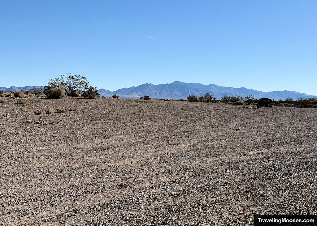 A large gravel parking lot with a lone abandoned salmon colored couch and mountains in the far distance