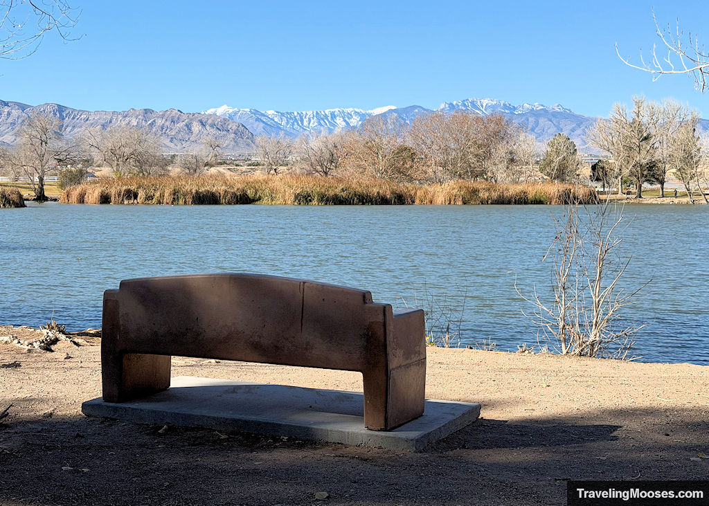 A park bench overlooking a nice lake overlooking rugged snowcapped mountains