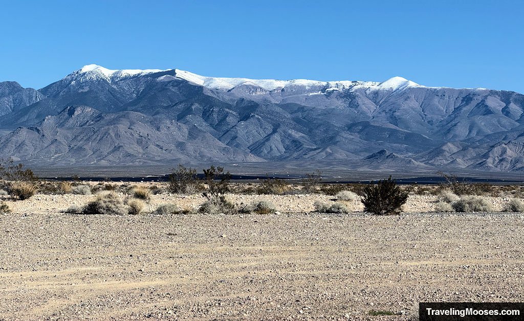 A gravel parking lot with a tall snow cappped mountain range in the distance