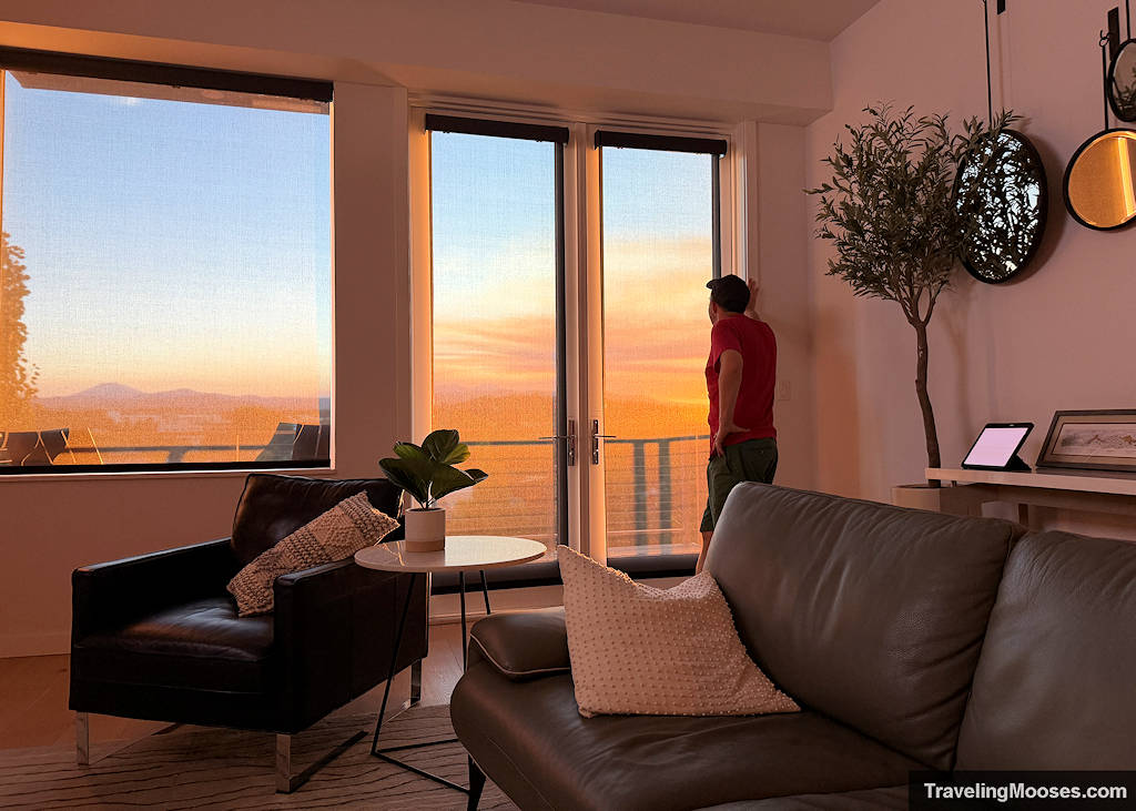 Man staring out a window over a balcony sunset