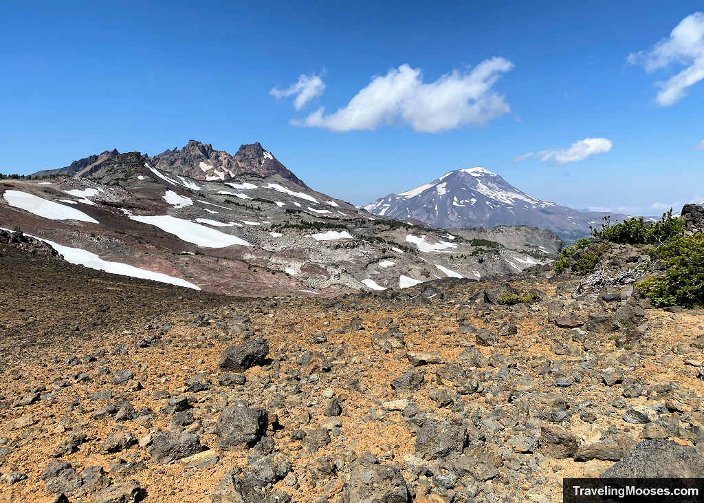 Wide rocky ridge view looking out toward Broken Top and South Sister with patches of lingering summer snow