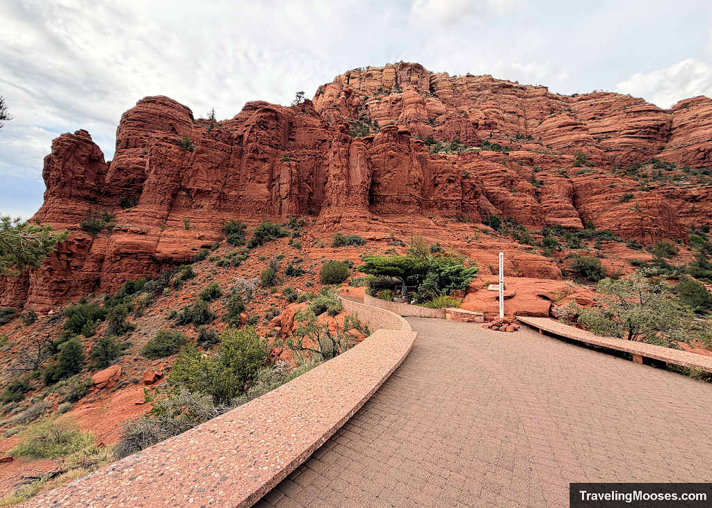 aved access ramp with low stone walls leading toward towering red rock cliffs at the Chapel of the Holy Cross in Sedona.