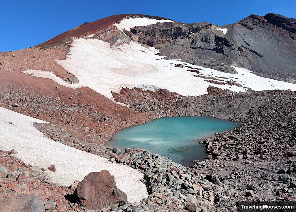 Blue glacier lake at the base of a large red volcano