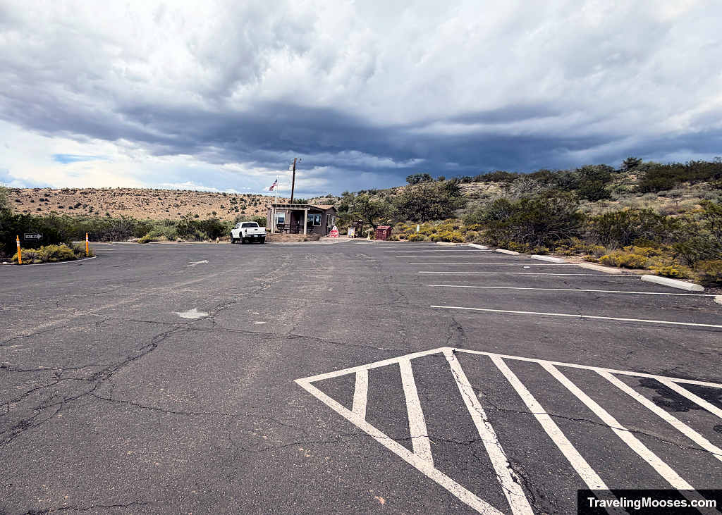 Paved parking lot and small park ranger station at the Montezuma Well trailhead under dark storm clouds.