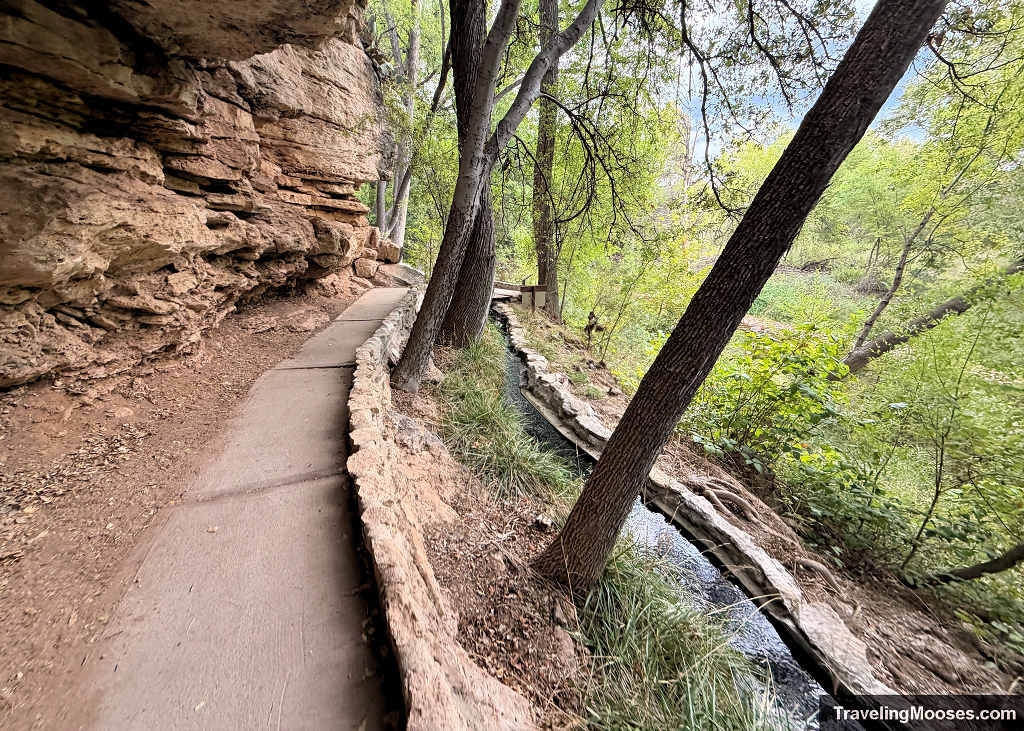 Paved walking trail beneath a limestone rock overhang running alongside the ancient stone-lined irrigation ditch at Montezuma Well.