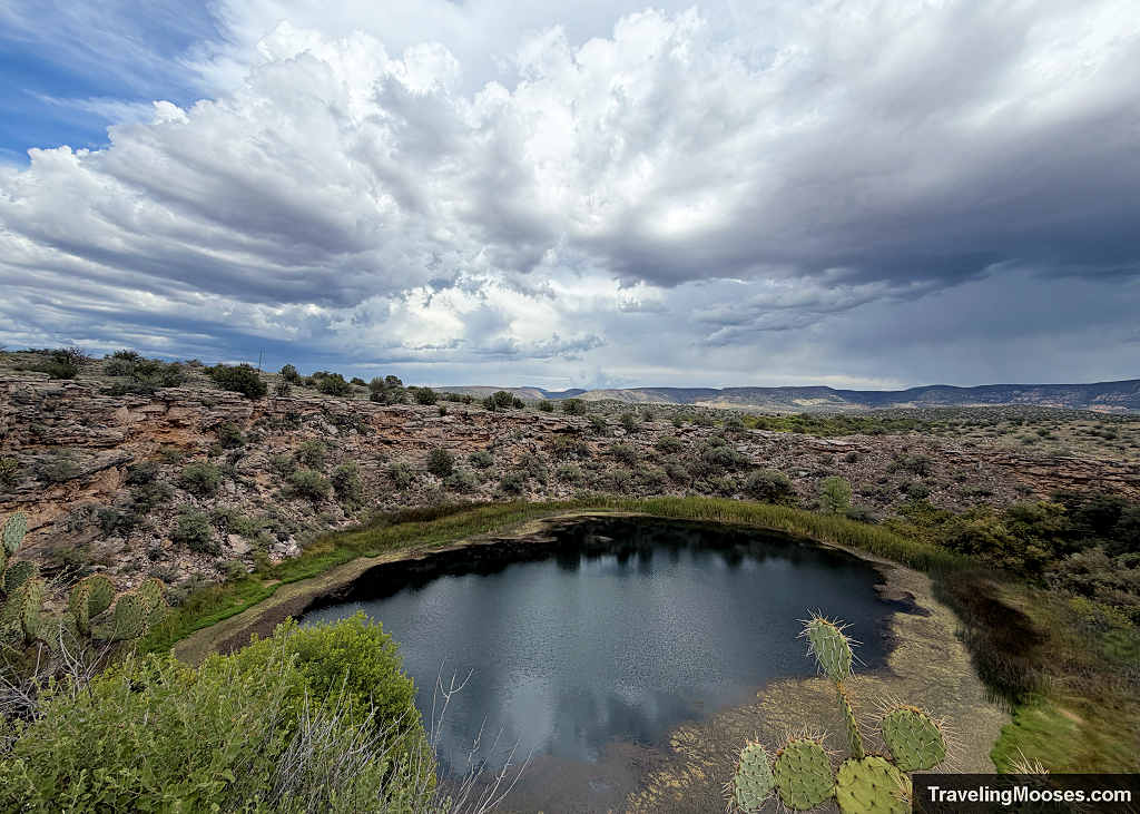 Dramatic storm clouds rolling over the vast limestone sinkhole and green spring water at Montezuma Well.
