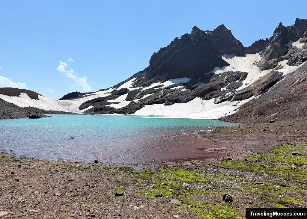Turquoise waters of No Name Lake below snowfields and the volcanic rim of Broken Top in Oregon