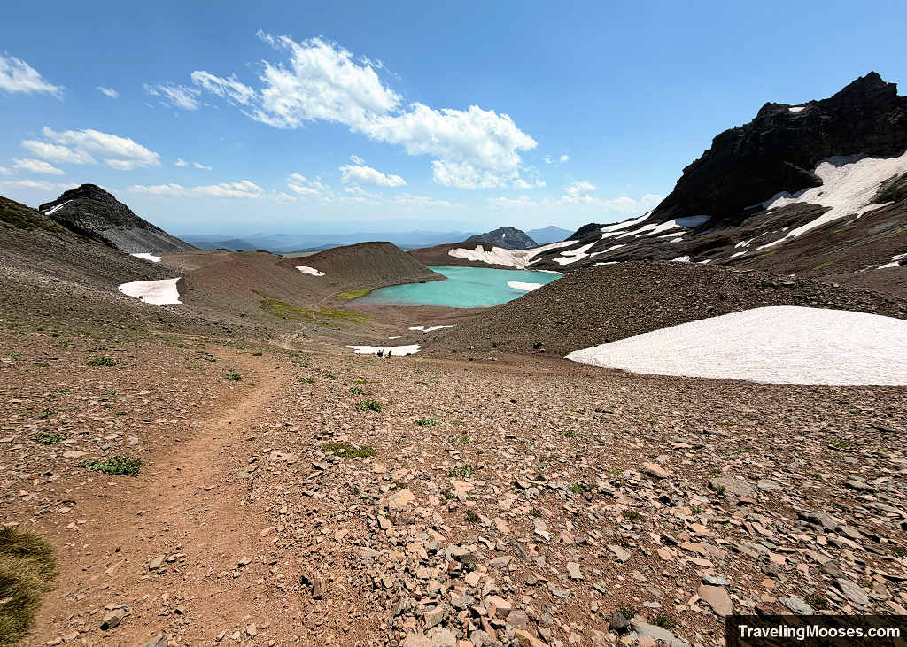 irt hiking trail descending an open volcanic scree slope toward the turquoise meltwater tarn below Bend Glacier
