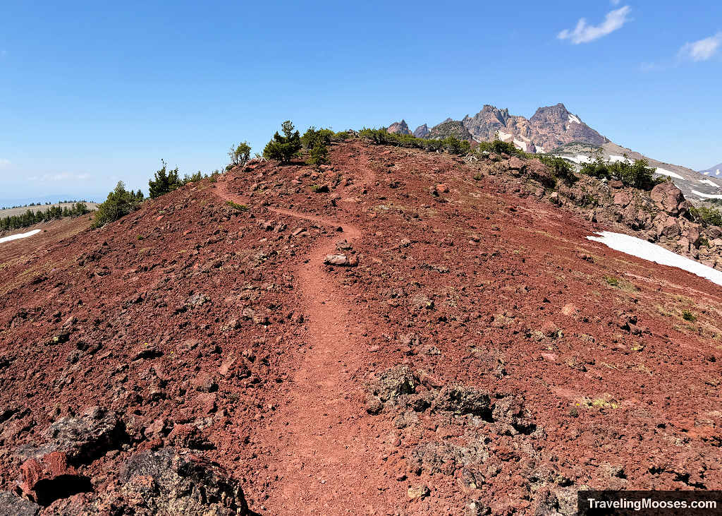 Red volcanic cinder trail climbing a ridgeline toward Broken Top along the route beyond Tam McArthur Rim