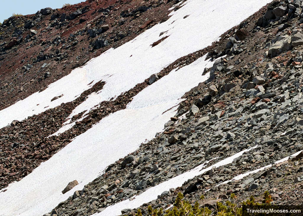 Steep lingering snowfield across red volcanic scree along the scramble route past Tam McArthur Rim toward Broken Hand