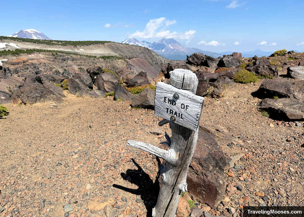 Weathered wooden End of Trail sign at Tam McArthur Rim overlooking volcanic terrain with the Three Sisters in the distance