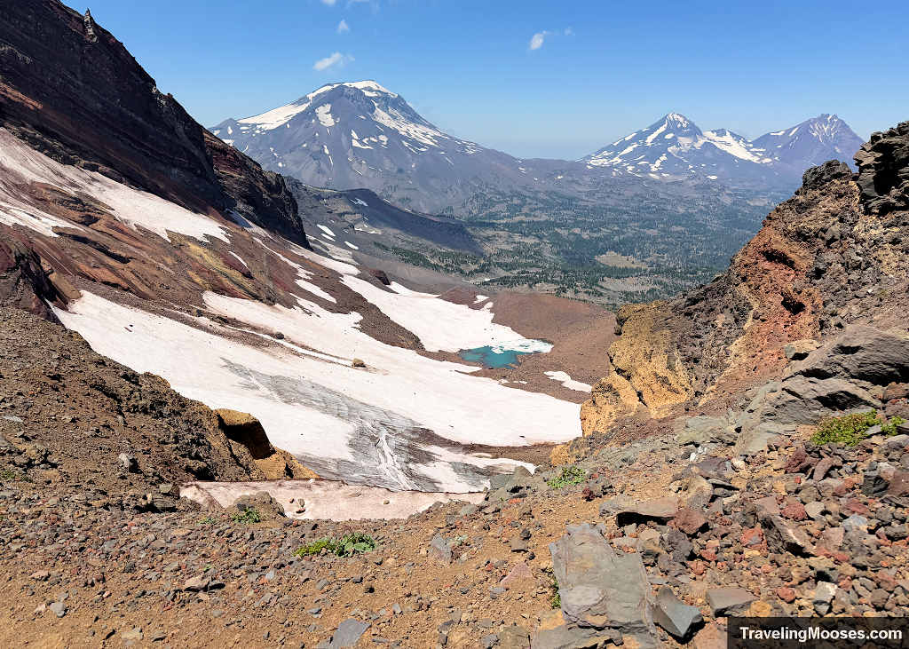 View framed by jagged volcanic canyon walls looking out across the glacial snowpack and Bend Glacier tarn toward South Sister