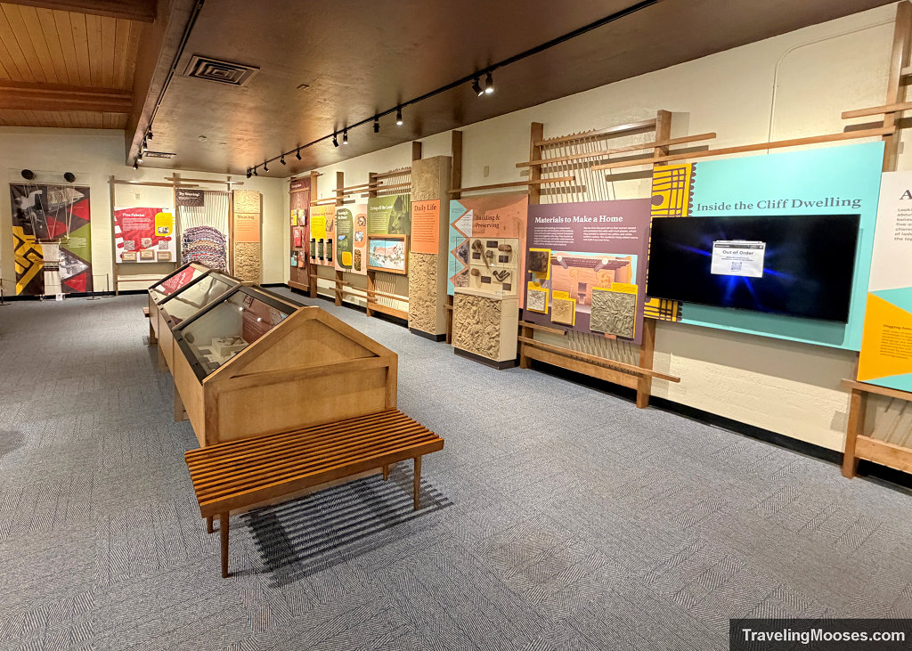 Indoor museum exhibits and interpretive wall displays inside the Montezuma Castle visitor center with wooden benches in the foreground