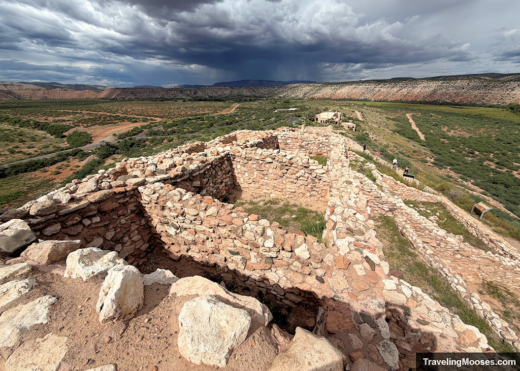 Wide panoramic overlook from the citadel rooftop across stone foundations and the Verde Valley under dramatic dark rain clouds