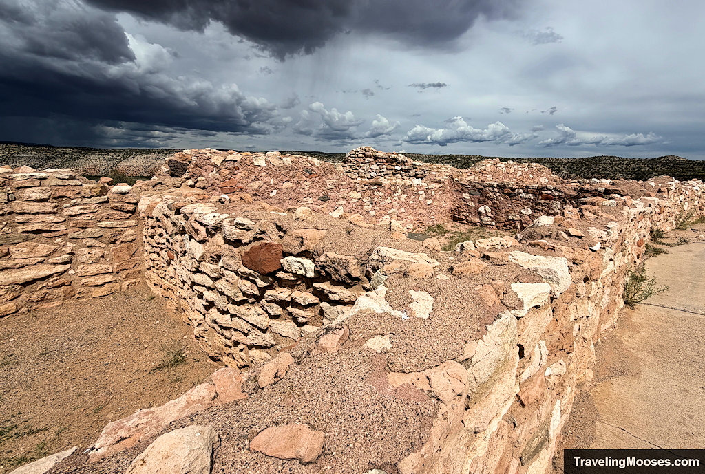 Close-up view of stacked limestone and sandstone masonry walls bordering a concrete walking trail under a stormy sky