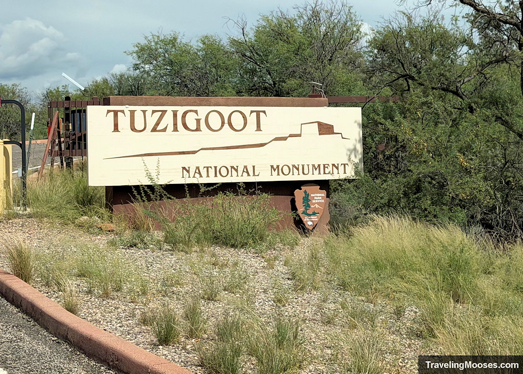 Brown and cream National Park Service entrance sign for Tuzigoot National Monument set along a desert hillside