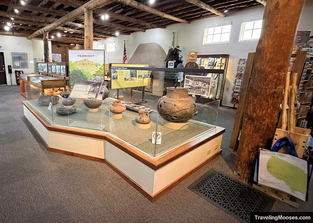 Glass museum display cases containing ancient pottery and artifacts beneath exposed wooden ceiling beams