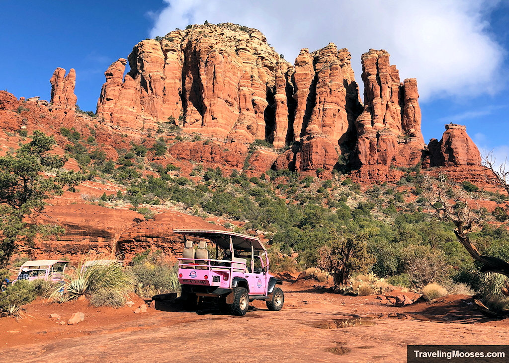 Pink Jeep tour vehicle parked on red slickrock beneath towering sandstone buttes