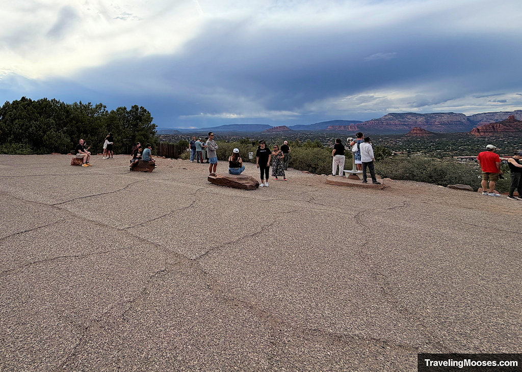 Visitors sitting on low red landscape boulders across the asphal