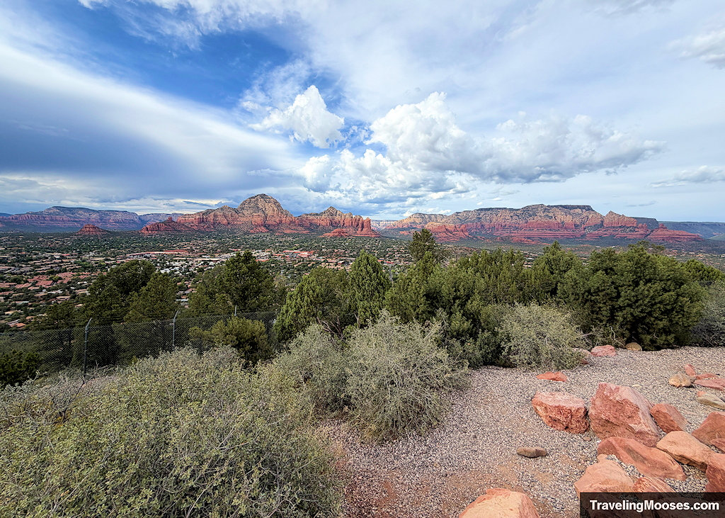 Looking out over the scrub brush, gravel slope, and chain-link fence towards Red Sandstone Mountains