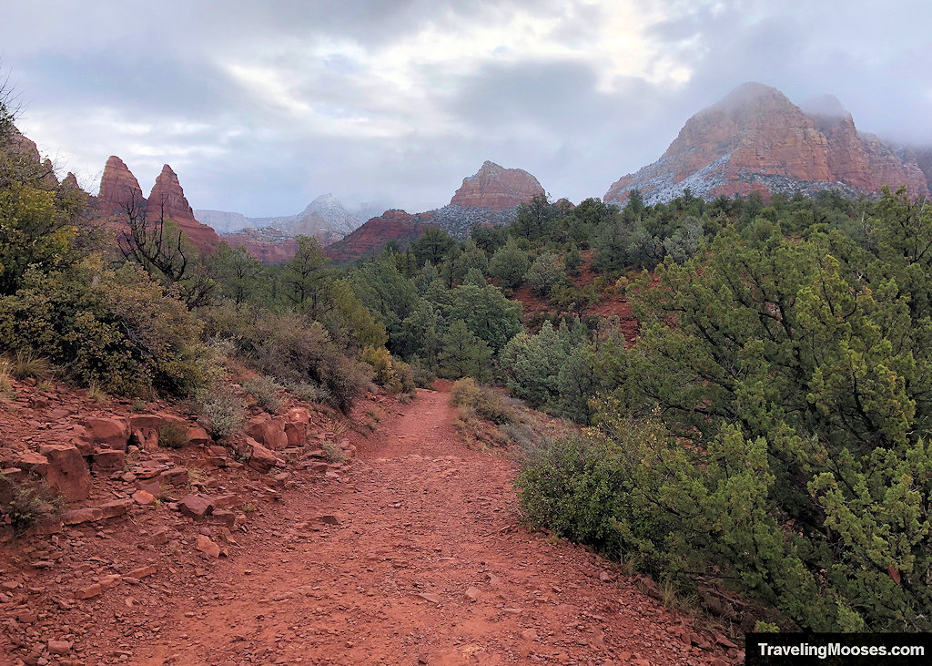 Red dirt path on Little Horse Trail winding toward misty sandstone peaks