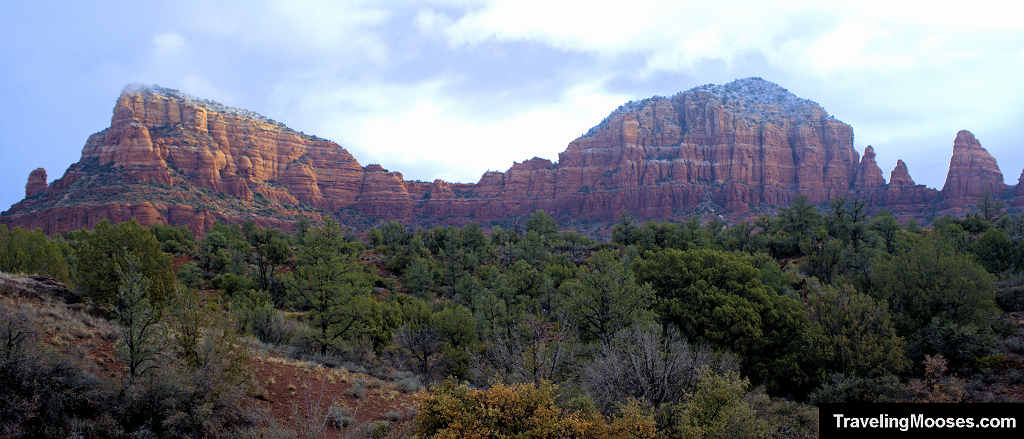 Panoramic view of the sprawling red rock sandstone ridgeline rising above a green valley