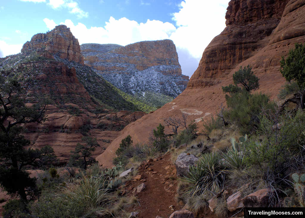 Narrow red dirt hiking trail leading along a brushy hillside toward the angled White Line slickrock bench