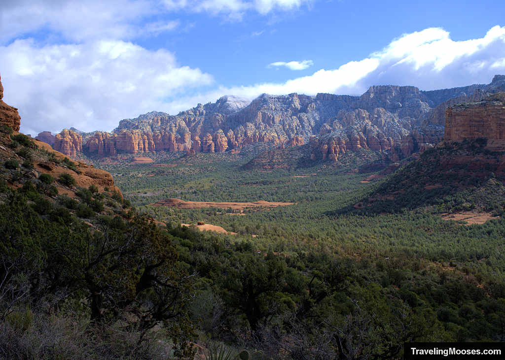 Sweeping elevated view of a wide forested valley bordered by snow-dusted red rock ridges
