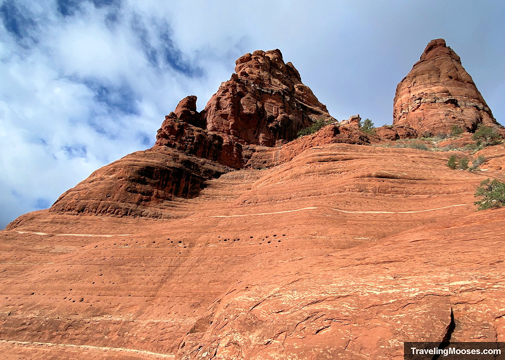 Upward-angled view of a steep red sandstone cliff face showing horizontal sediment bands