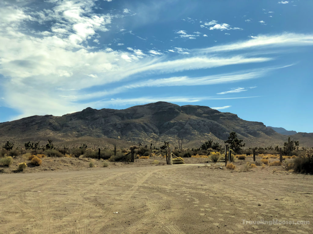 Dirt road leading through a decaying fence towards some rugged mountains.