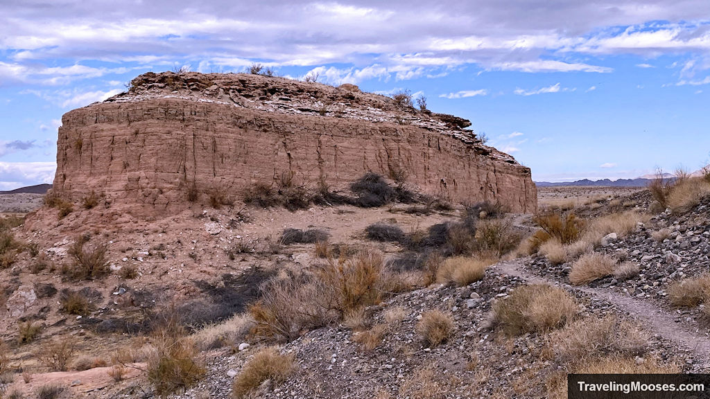 A large rock formation with a wandering path through the desert.