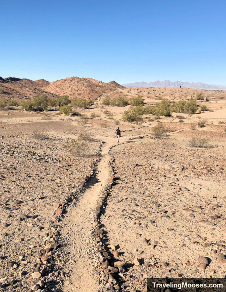 Man walking down disc golf course with mountains in the background