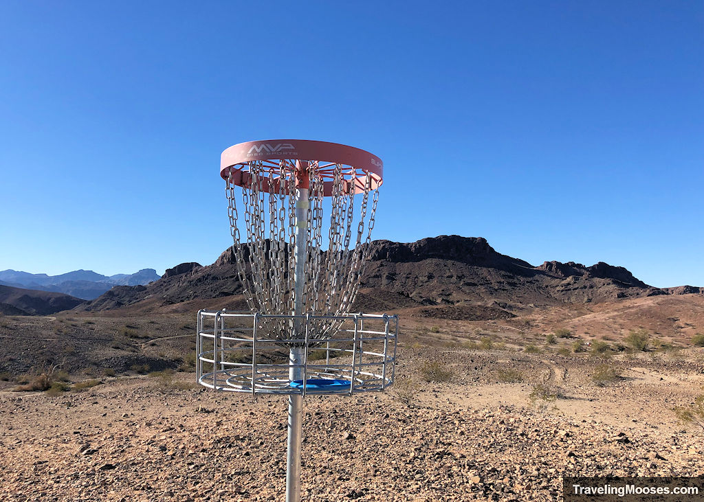 disc golf basket with a red rim in front of a desert mountain landscape