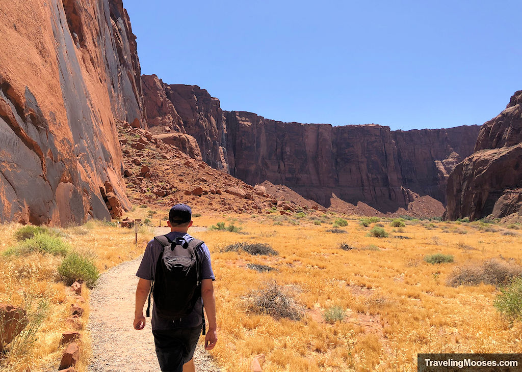 Man walking down a gravel path towards large canyon walls