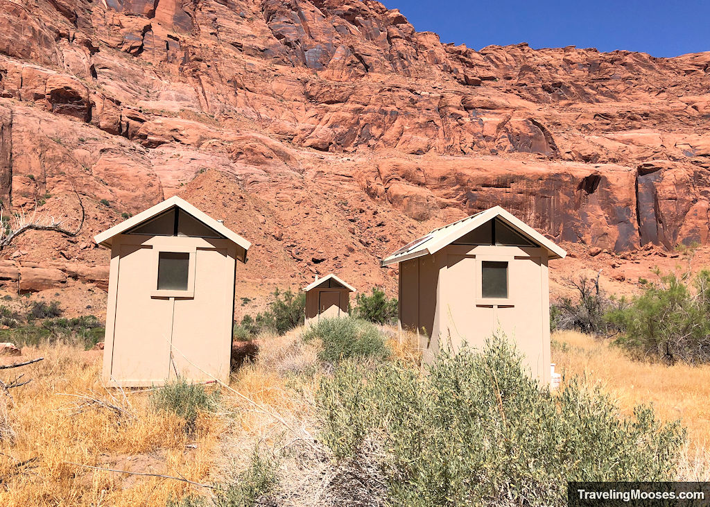 Four cream colored outhouses in front of a large reddish canyon wall