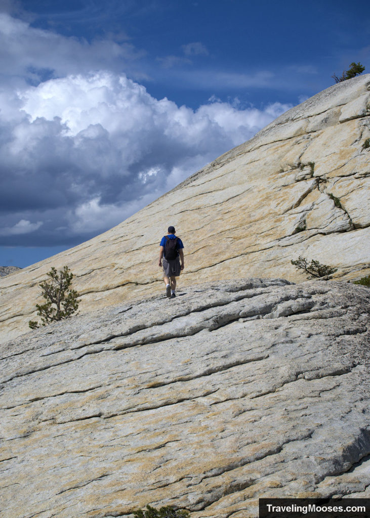 Man walking up granite dome towards the summit of Lembert Dome
