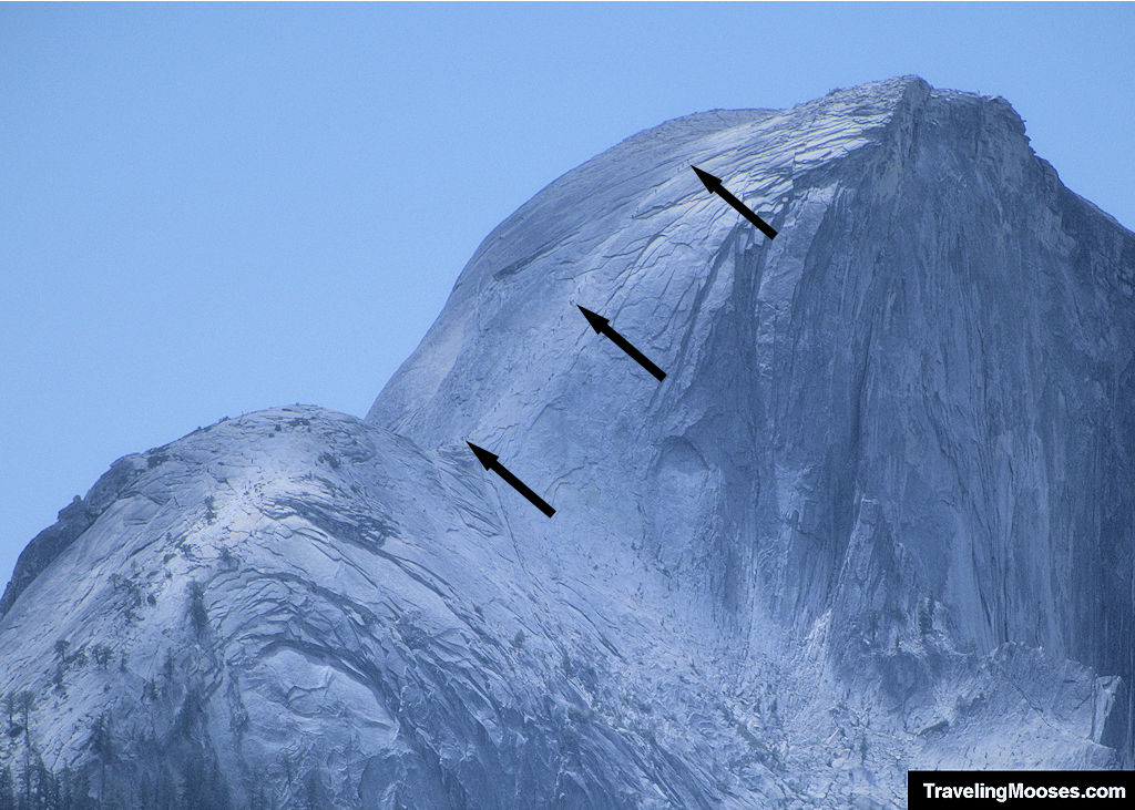 A zoomed in Half Dome with hikers traversing up the cables