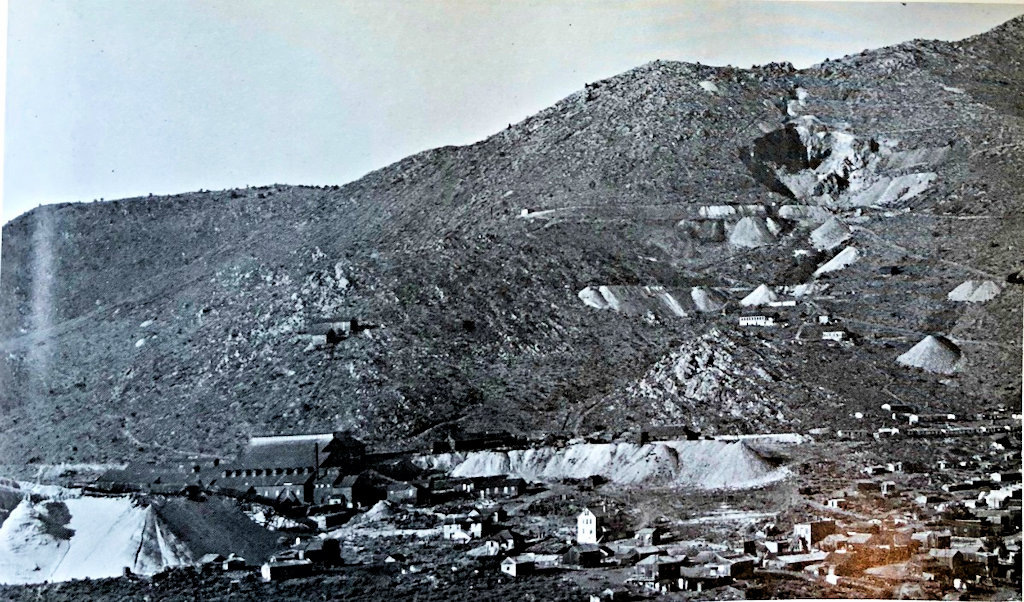 Black and White photo of a Mining camp from the 1890s in Delamar, NV. Small structures and paths carved into the mountainside are seen.