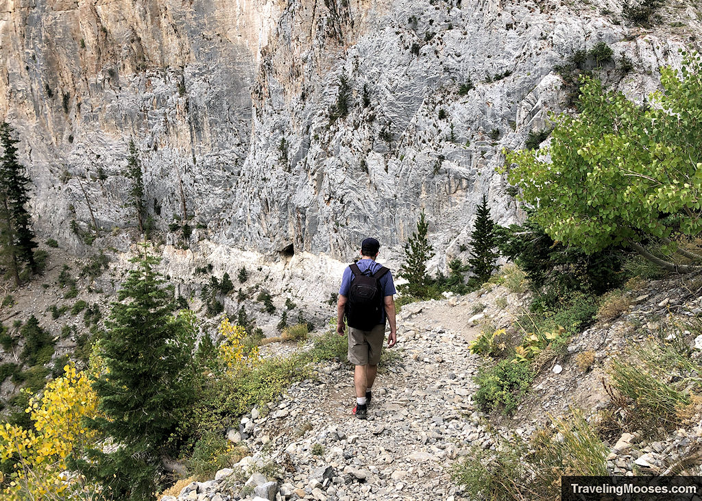 Man walking down a rocky path towards a cave carved in the stone cliffs