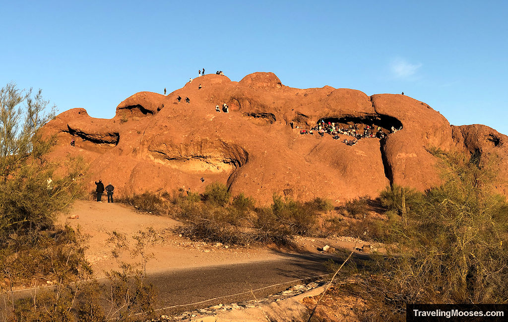 A large sandstone rock formation with crowds of visitors covering a large area of it