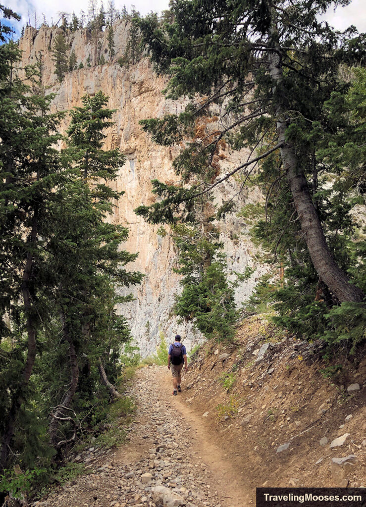 Man walking on trail towards rocky cliff