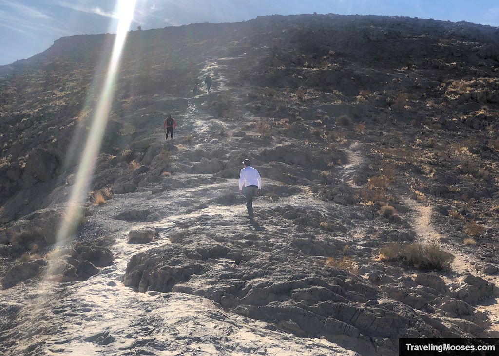 People walking up a rough trail towards a false summit on Lone Mountain Peak