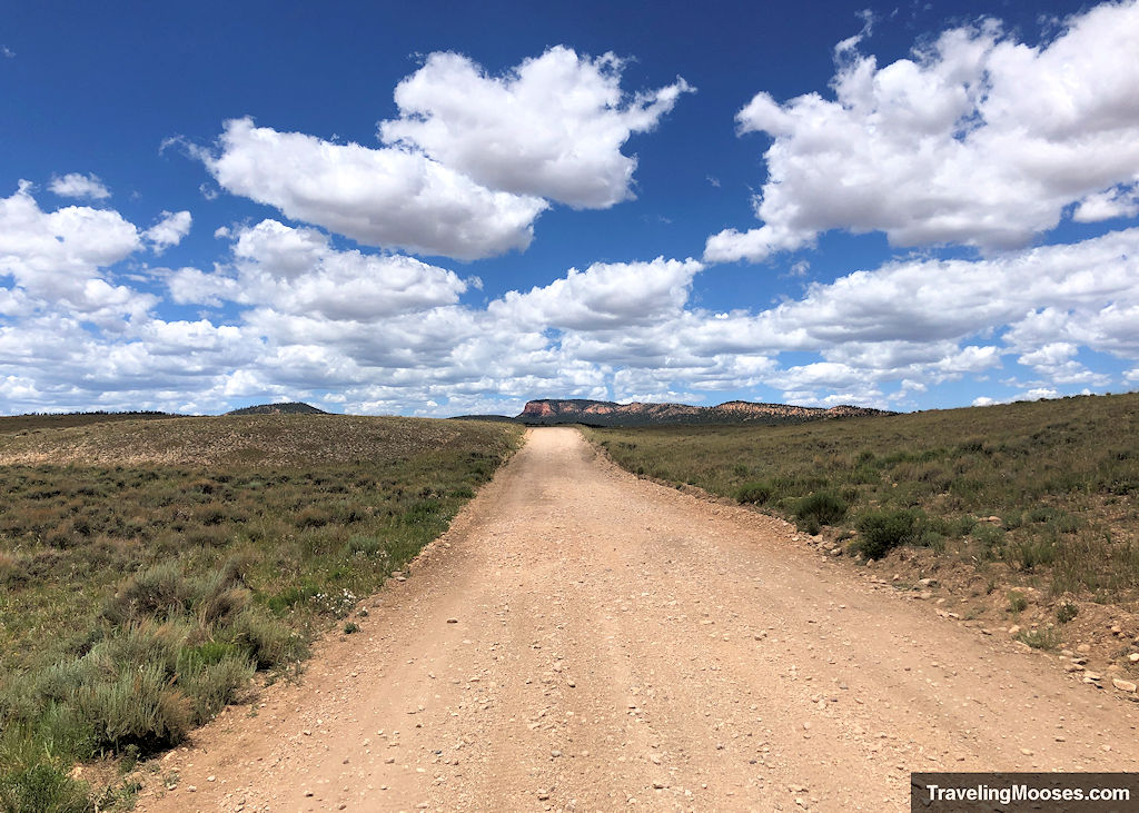 A long gravel road with rugged mountains seen in the distance