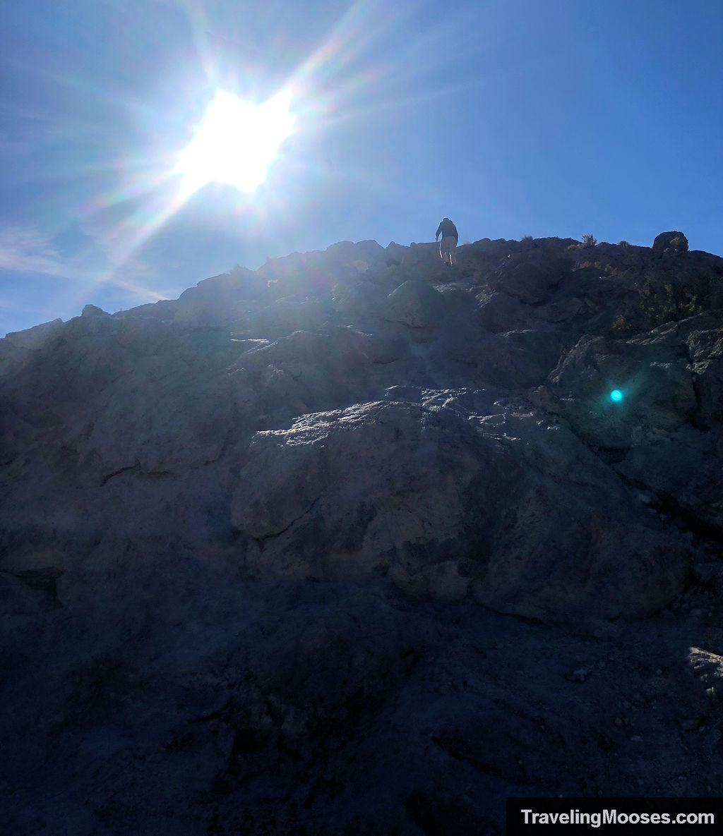 Man walking up a steep incline towards Lone Mountain Peak's summit