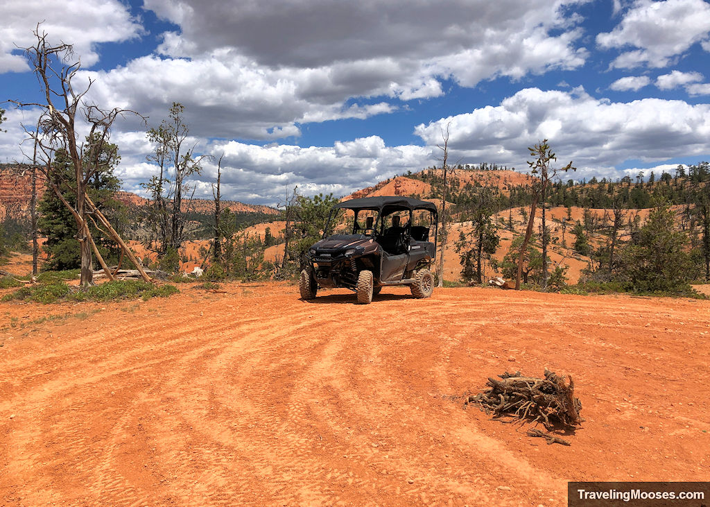 An all-terrain vehicle parked on dark red dirt in front of a reddish colored hills on a stormy day