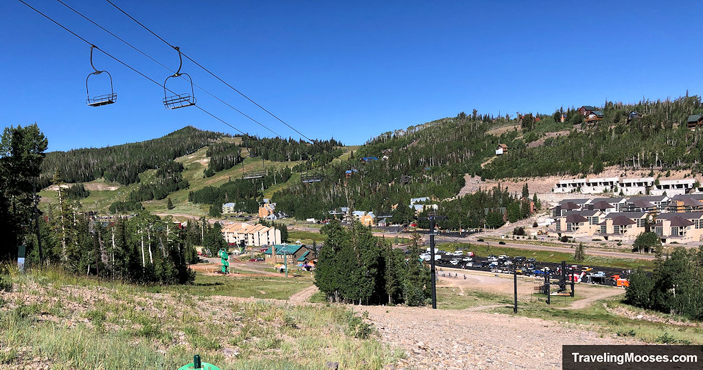 View of the Giant Steps base area at Brian Head Resort with chairlifts, lodges, and parking visible on a clear summer day.