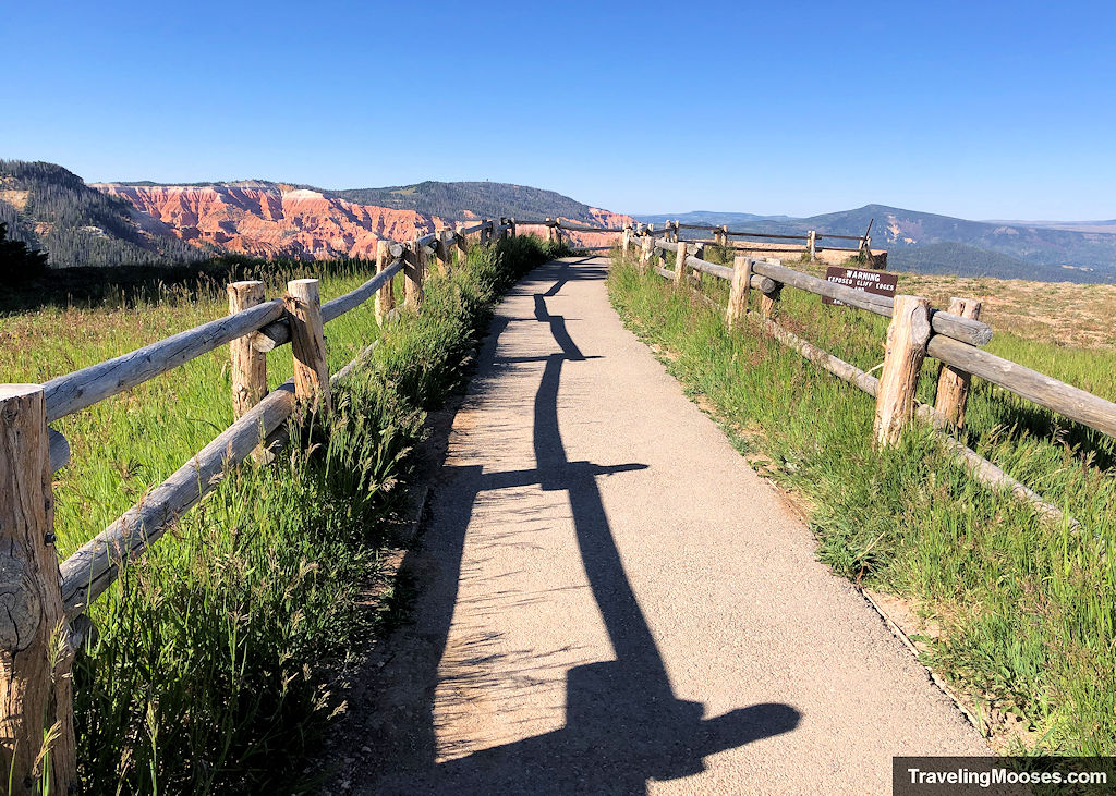 Paved walkway lined with wooden fencing at the North View Overlook, with the Cedar Breaks amphitheater visible in the distance.