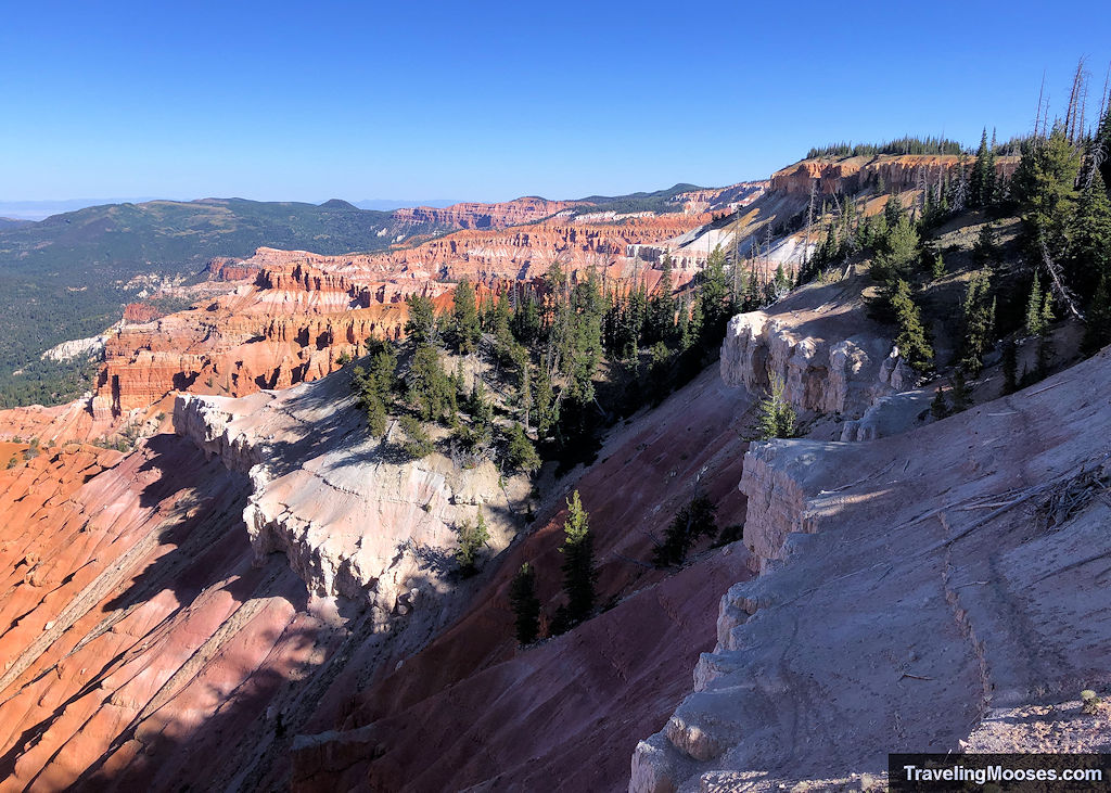 Railed viewing platform and log bench at the Sunset View Overlook in Cedar Breaks, with distant cliffs in the background.