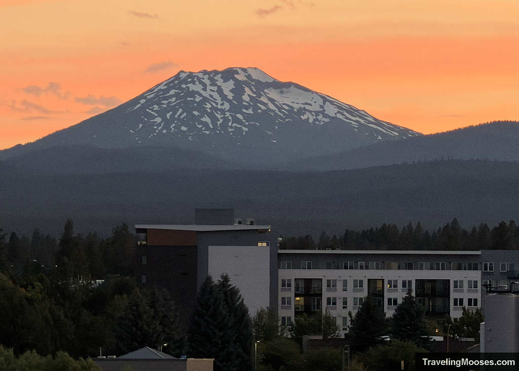 Sunset over modern lodging buildings in Bend Oregon with snow-dusted Mt. Bachelor glowing in the background.